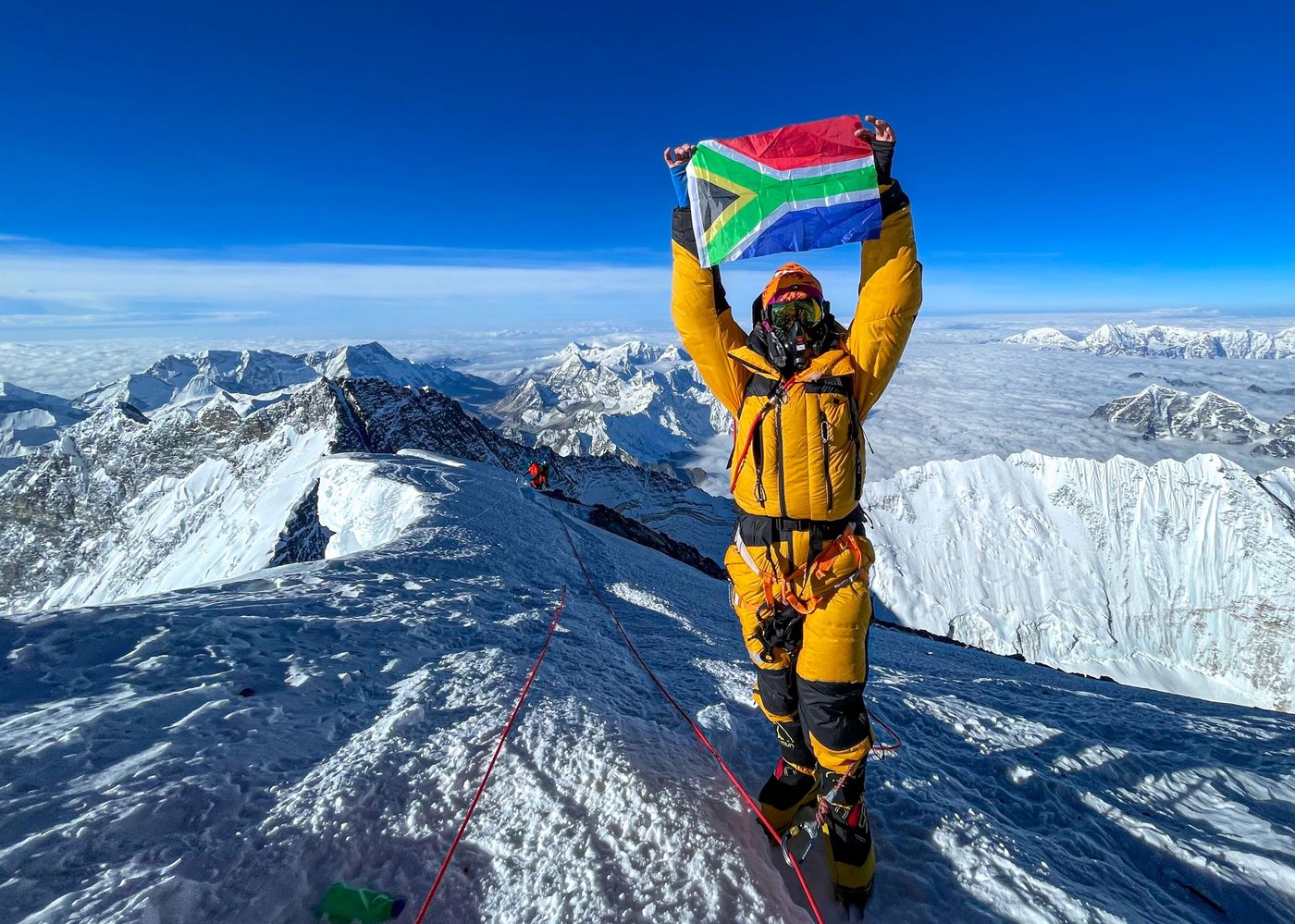Climber holding the South African flag on a high summit above the clouds